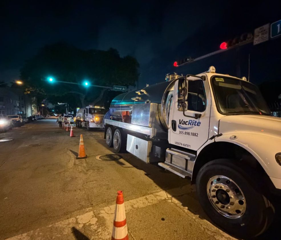A VacRite tanker working a Miami Beach street after dark with traffic cones set out and a second truck staged up the block