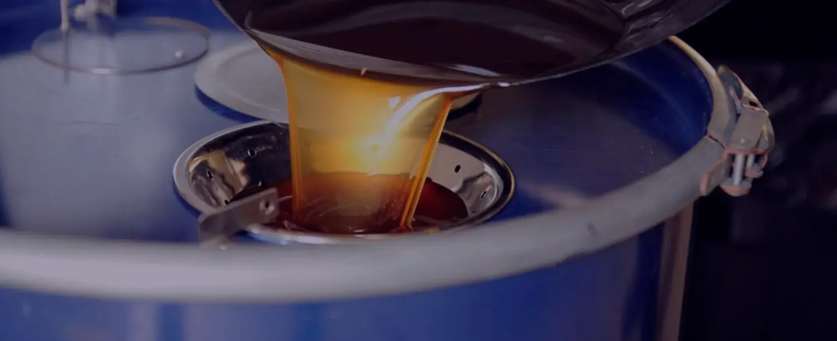 Used cooking oil pouring in a thick amber stream into a blue collection drum